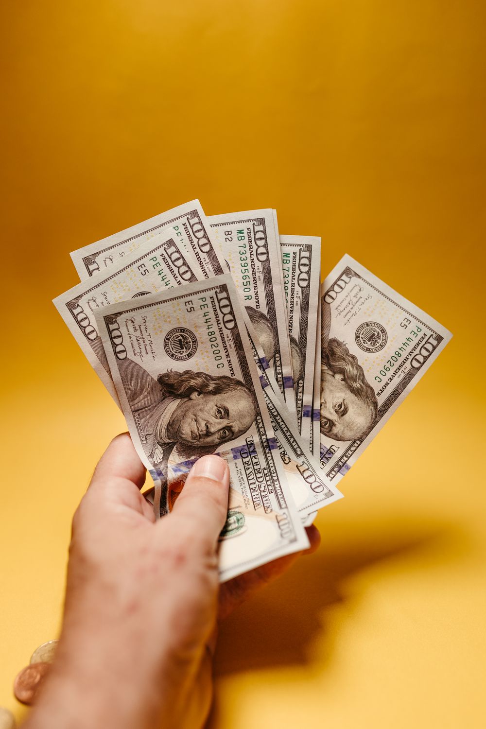 Close-up of a hand holding US dollar bills with a yellow backdrop.