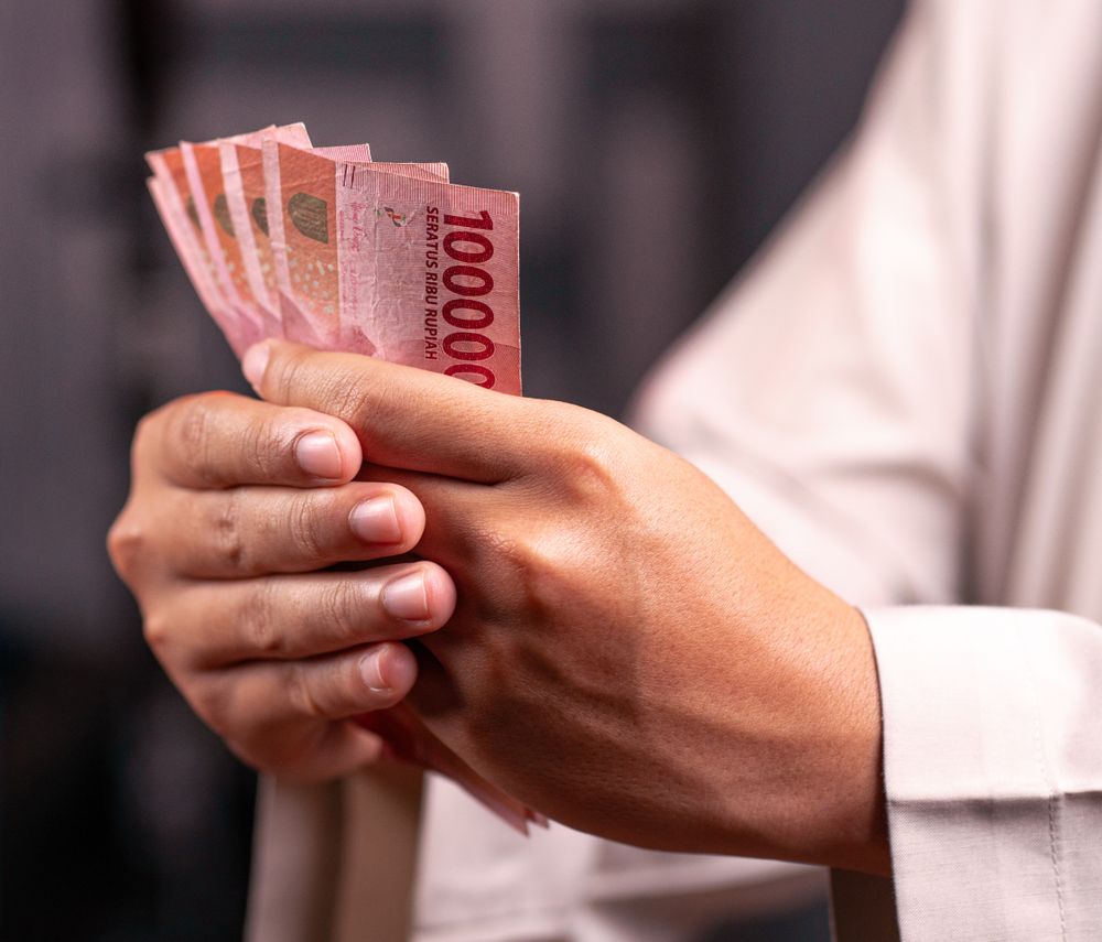 Close-up of hands holding Indonesian Rupiah 100,000 bills, highlighting financial and economic concepts.