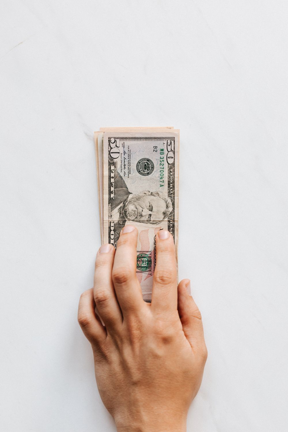 Top view of crop faceless person investing pile of American dollar banknotes on white table