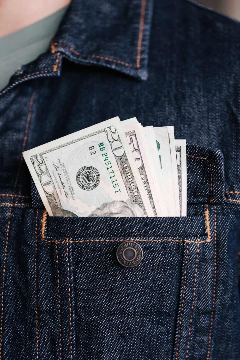 Unrecognizable male in jeans jacket with diverse American dollars sticking out of pocket