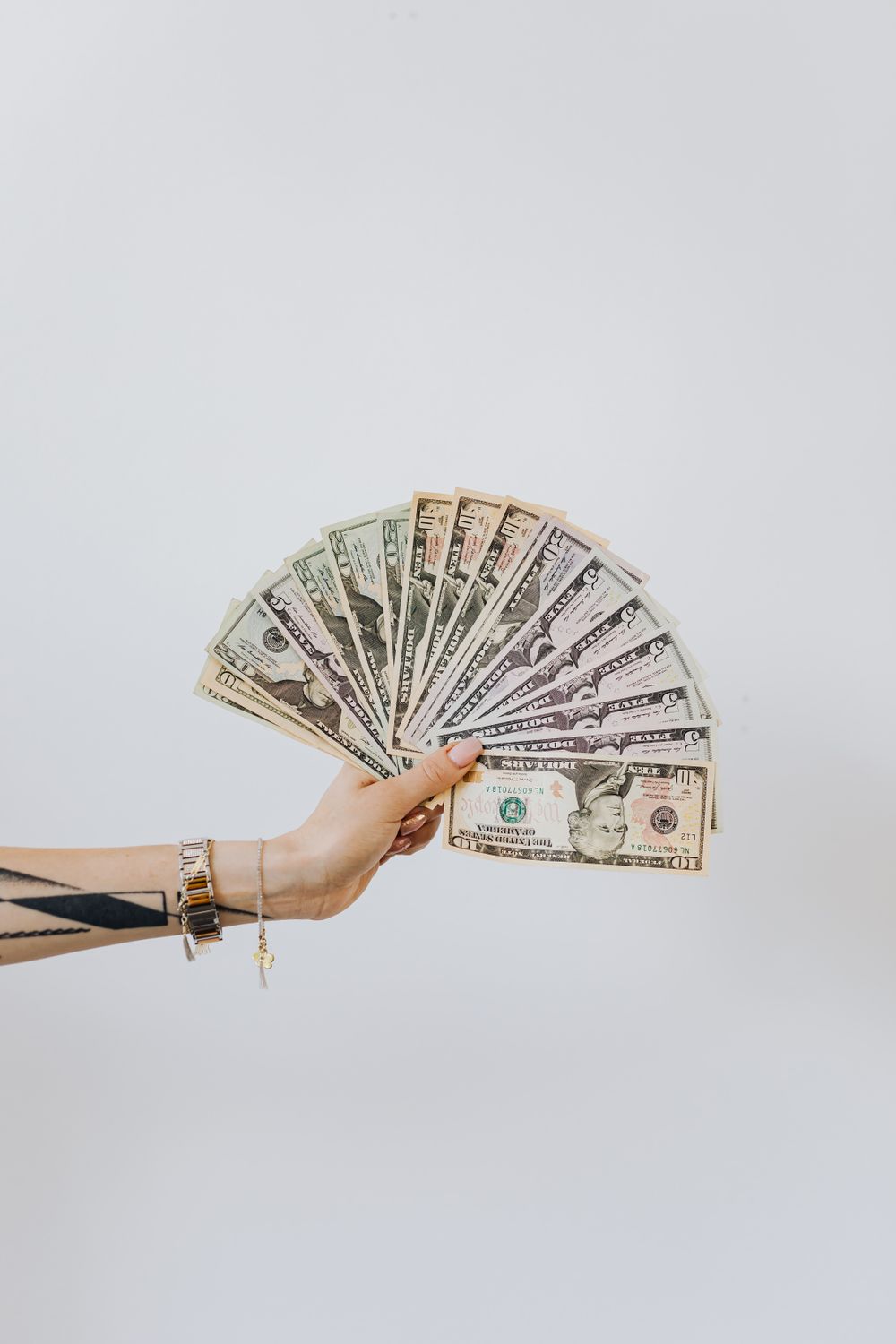 Close-up of a hand displaying fanned out US dollar bills against a white background.