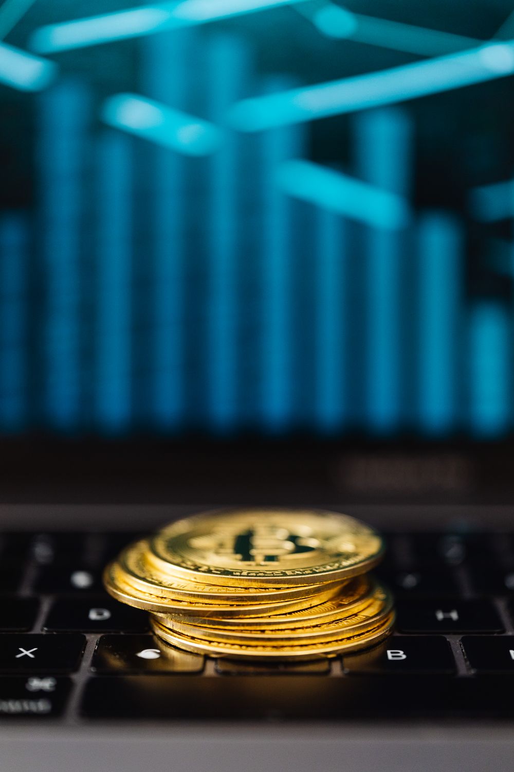 Close-up of gold Bitcoin coins stacked on a laptop keyboard with a digital chart reflection.